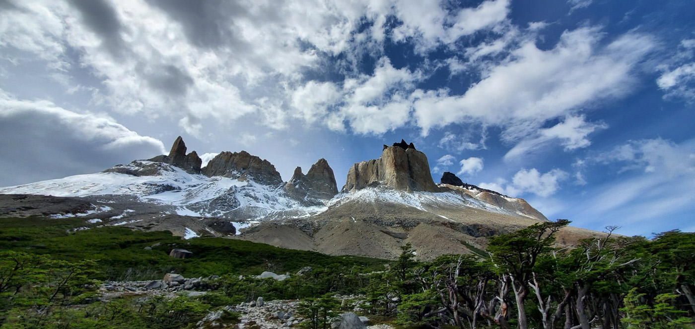 Snow-streaked granite towers of the Torres del Paine massif above a bank of low scrub, under broken cloud.